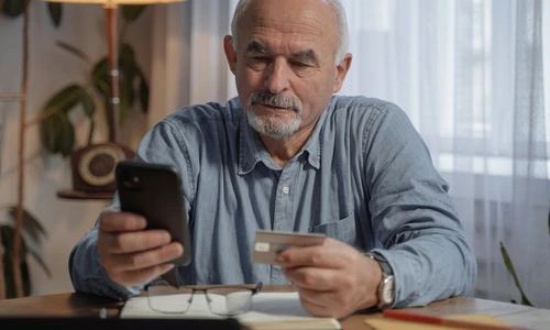 un barbat in varsta se uita pe un telefon mobil tinand in amna un card de credit jpg